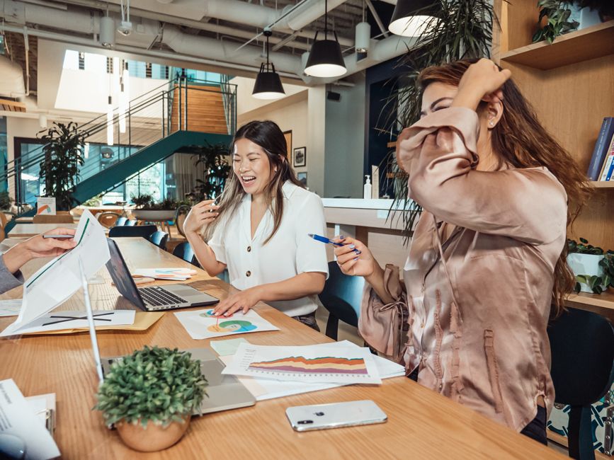 Professional women collaborating during a lively office meeting, surrounded by technology and documents.