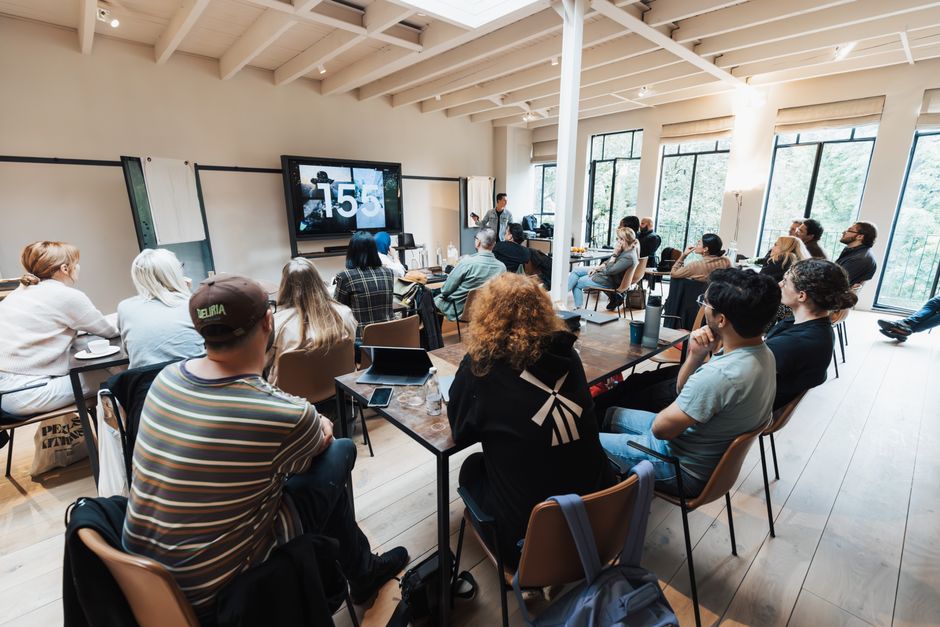 Diverse group attending a seminar in a modern wooden interior, focusing on a large screen presentation.