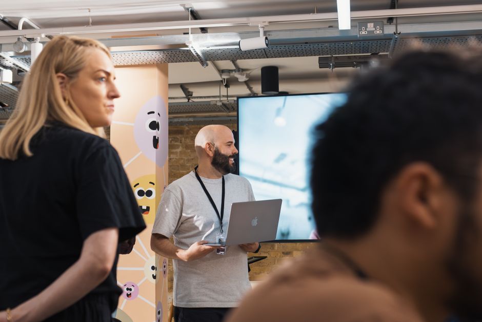 A team meeting with multiple adults in a modern office, featuring a presenter with a laptop.