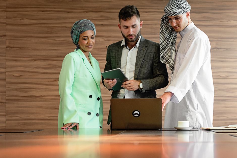 Three professionals in traditional and modern attire collaborate on a project in a contemporary office setting.